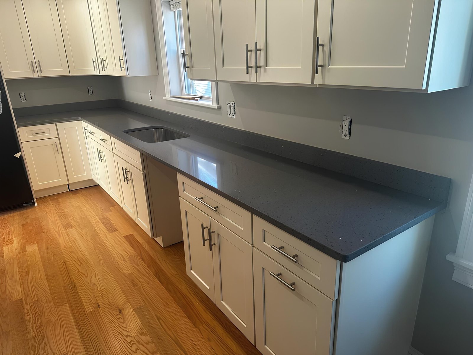 A modern kitchen featuring white cabinets and a sleek black countertop, showcasing Marble and Granite Services